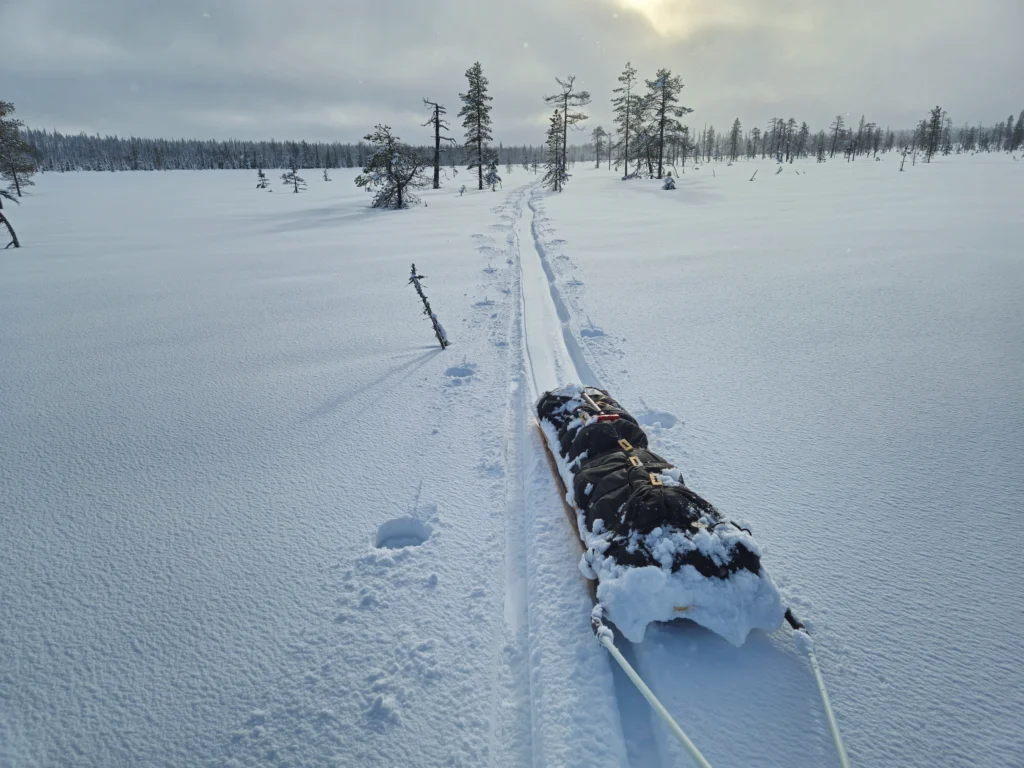 JR-27 Ahkio hiihtäjän perässä kuvattuna ison aapasuon seljänteellä, perässään hiihtäjän tekemä latu.
